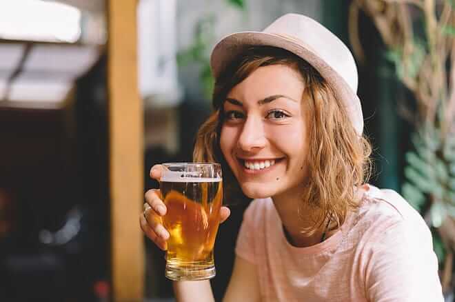 mulher jovem com chapéu tomando cerveja e sorrindo
