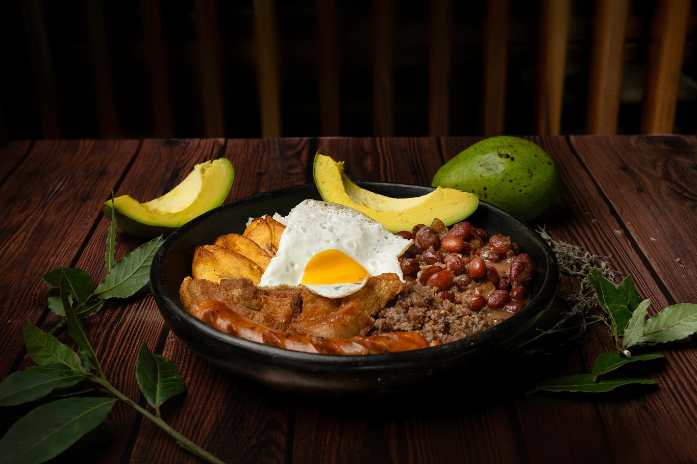 Comida típica colombiana, de antioquia, com feijão, ovos, arroz, torresmo, abacate e chouriço em prato na mesa marrom