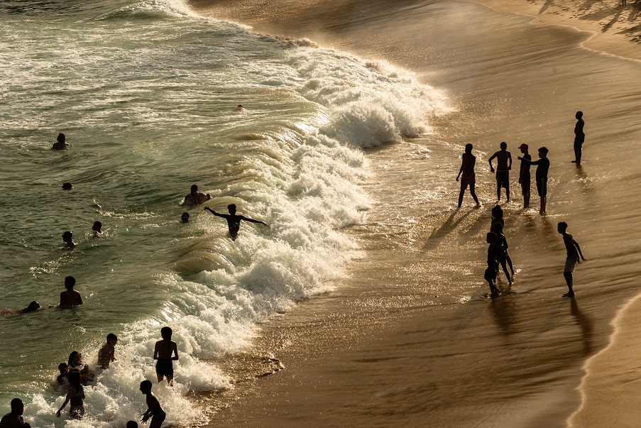 Praia com ondas com pessoas se divertindo ao pôr do sol
