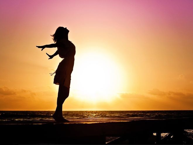 Exemplo de foto de silhueta de mulher posando na praia ao por do sol com os braços abertos