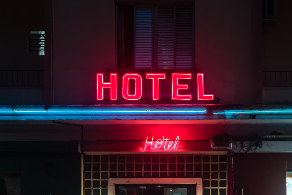 Fachada de hotel com letreiro neon em vermelho escrito "Hotel".