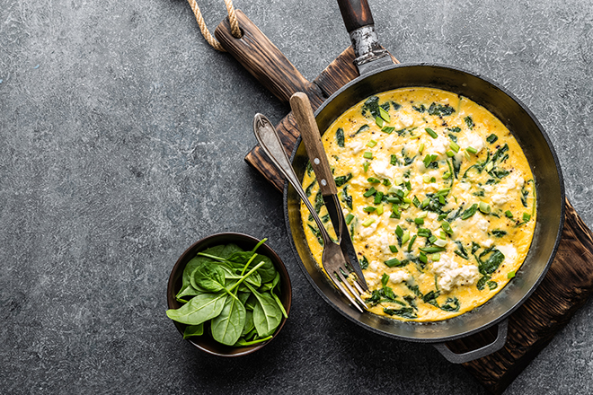 omelette with spinach and cheese in a pan on the concrete background top view