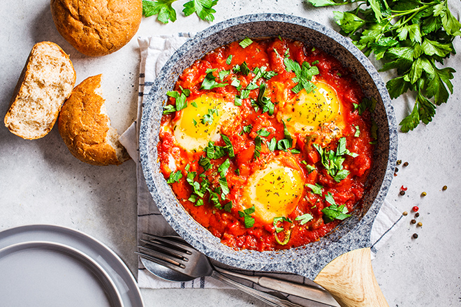 Traditional shakshuka in pan. Fried eggs in tomato sauce with herbs, top view.