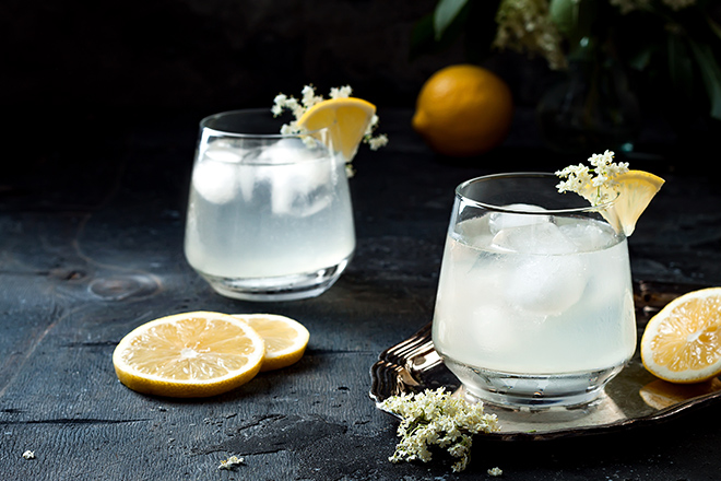 Two glasses of homemade elderflower gin sour or lemonade garnished with freshly picked elderflowers.
