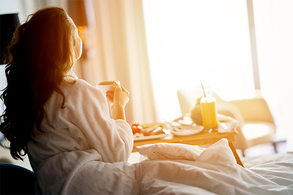 A lady sitting on a bed in the morning sun with breakfast