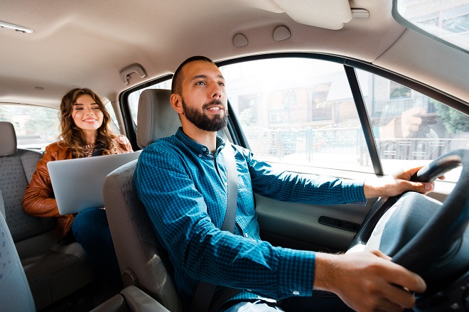 Alt-text: Motorista sorridente conversando com passageira. Mulher usando laptop em segundo plano