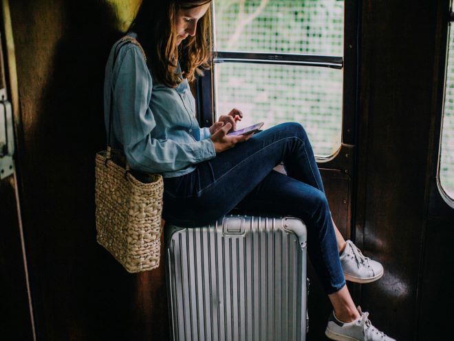 mulher mexendo no celular sentada em cima da mala em plena viagem