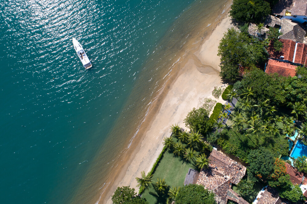 Imagem aérea de uma praia com casas na beira da areia e um barco no mar.