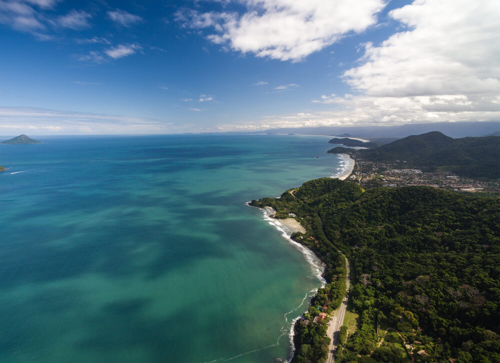 Imagem aérea de um litoral repleto de arvores e natureza.