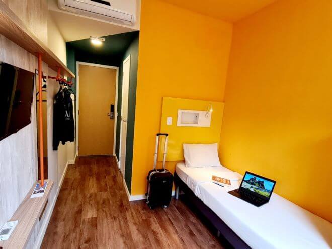 quarto de hotel ibis budget Petropólis com paredes amarelas e verdes , mala, notebook e casaco pendurado no armário 