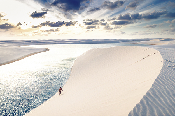 Person walking up a sand dune against a cloudy backdrop