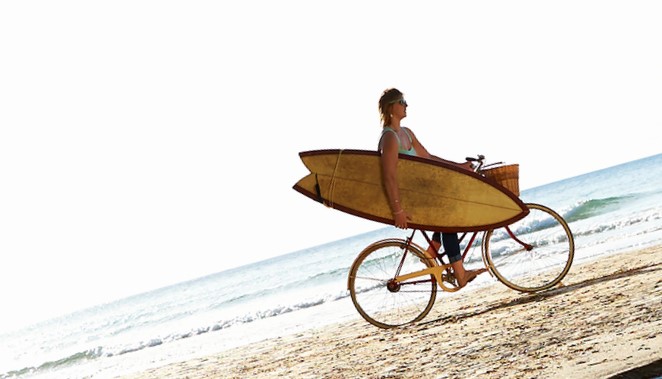 woman with surfboard on bike