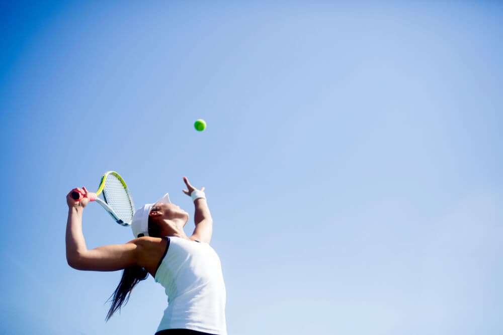 mulher com raquete de tênis na mão jogando bola de tênis para o alto em movimento de saque