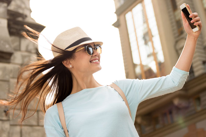 Foto de una mujer con sombrero y lentes de sol sacandose una selfie.